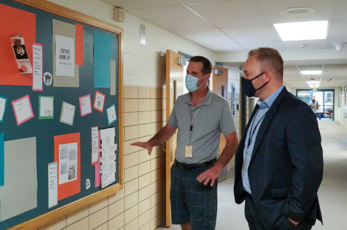 Superintendent Kinglsey talks with a staff person as they look at a school bulletin board. 
