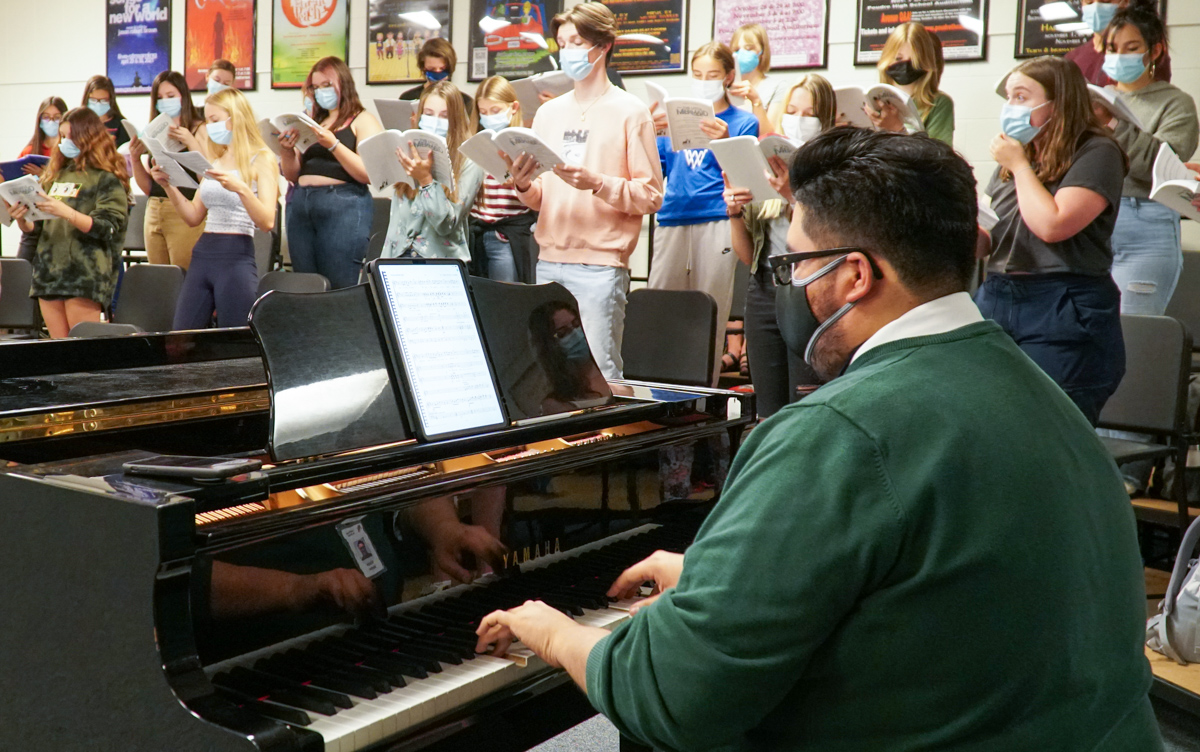 A music teacher plays the piano while student sing. 
