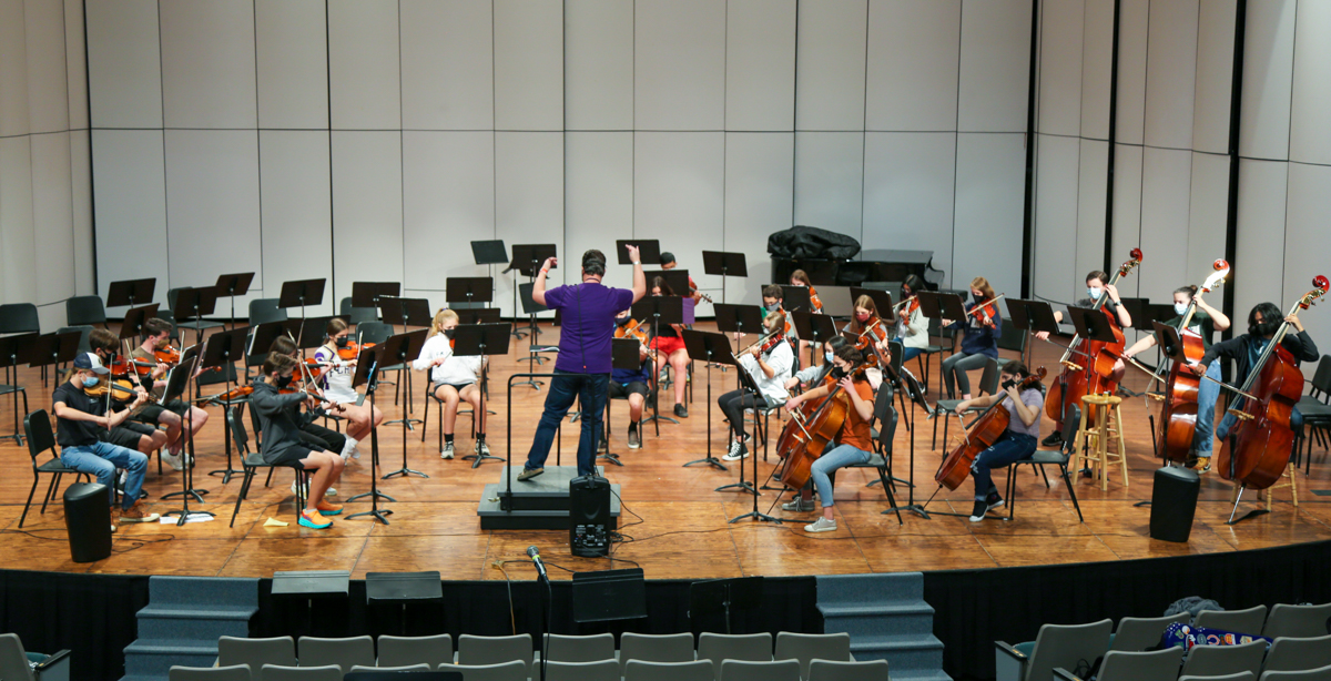 An orchestra rehearses on stage. 