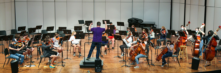 A high school orchestra rehearses on stage.