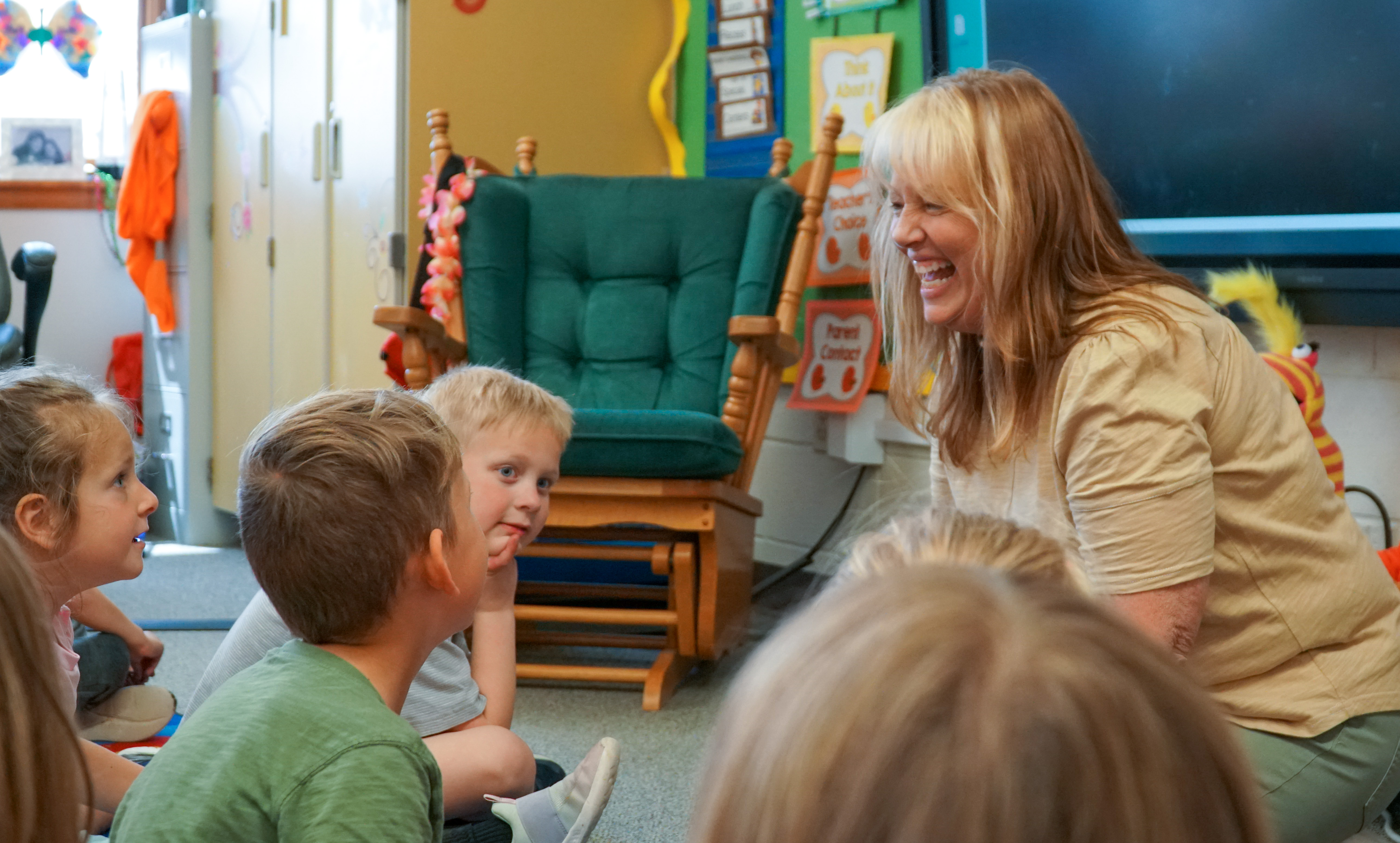 Bacon kindergartener teacher laughs with her students sitting on the floor. 