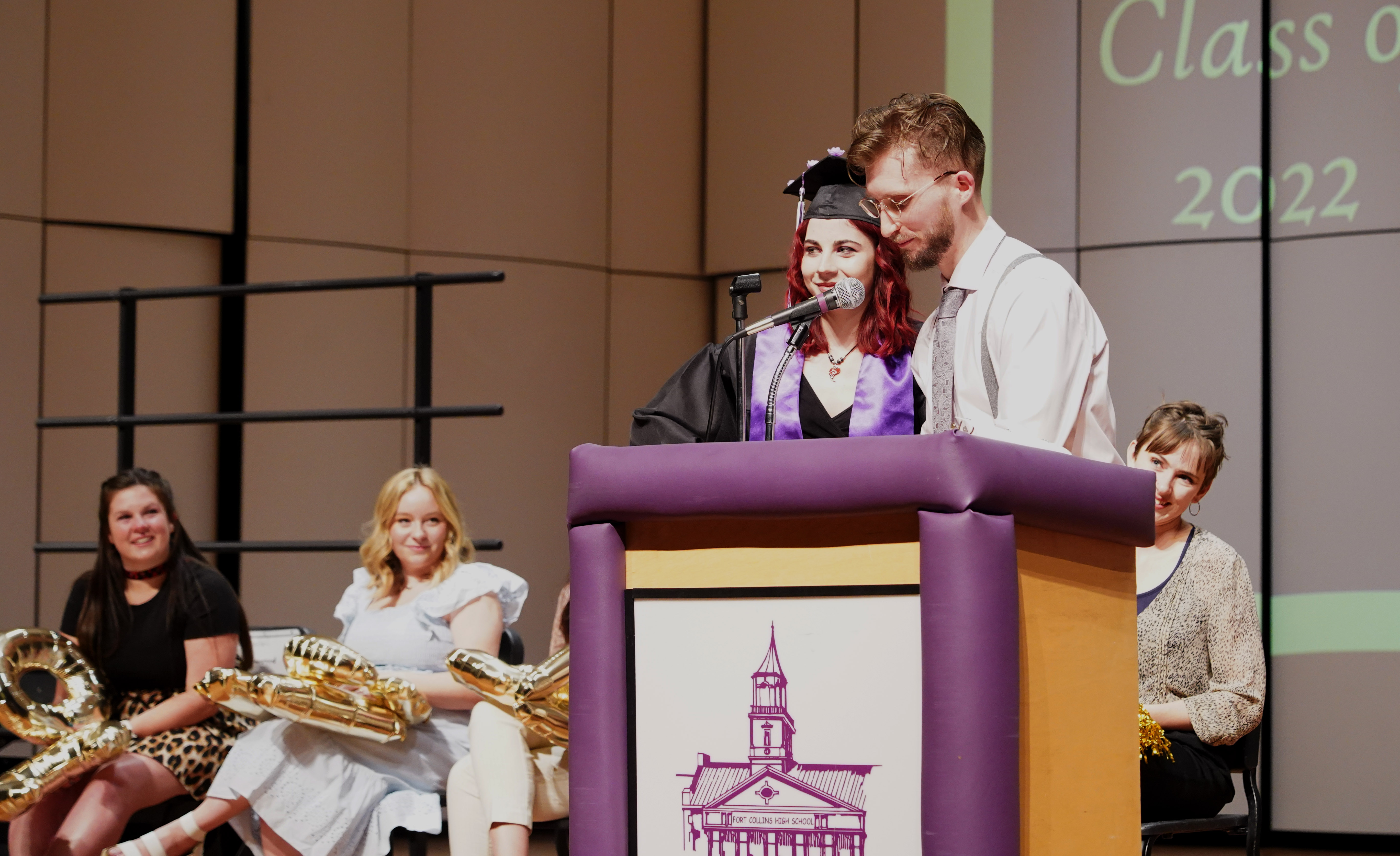 Two people at the podium with graduates in the background.