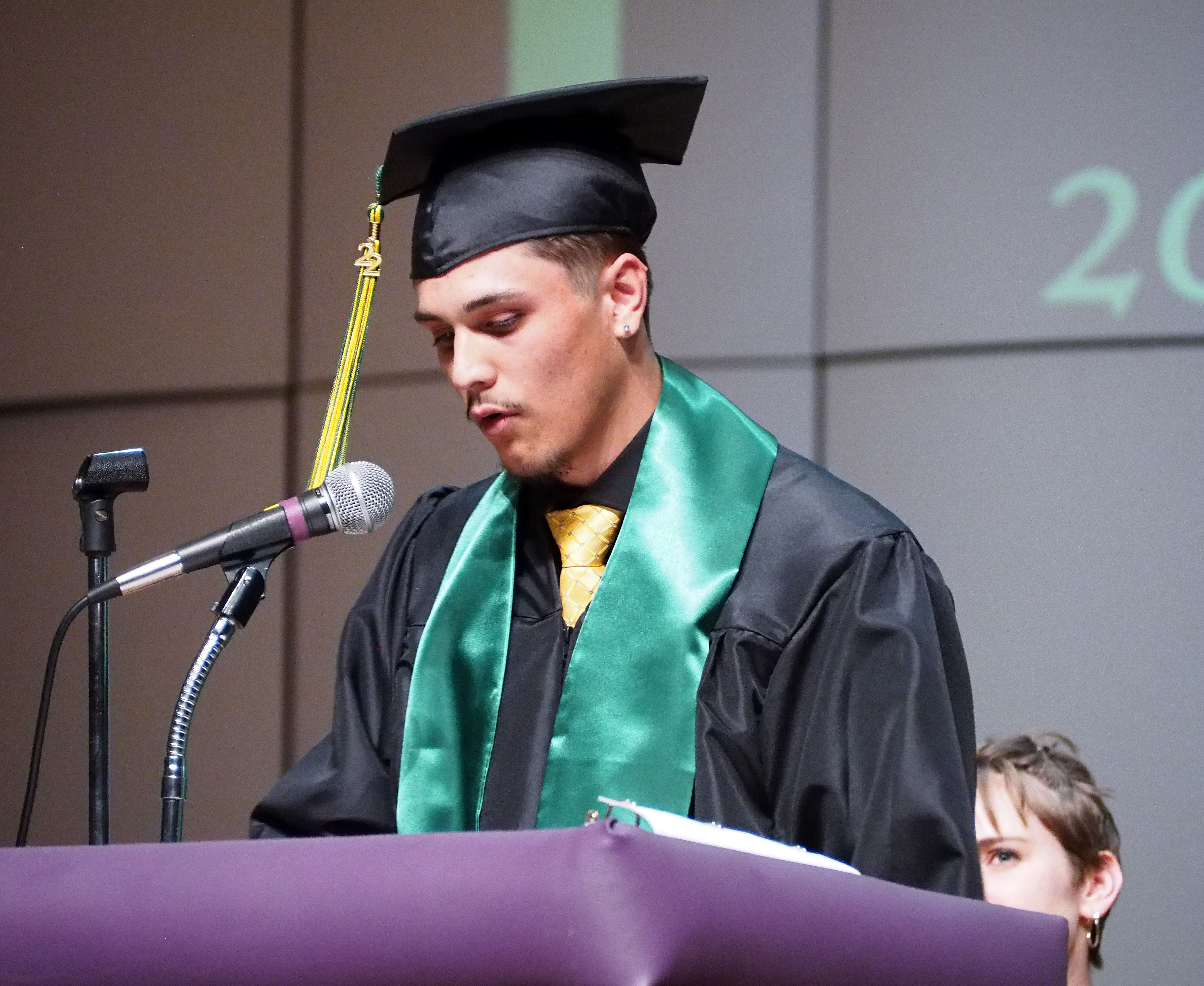 A male graduate with a sash speaks at the podium