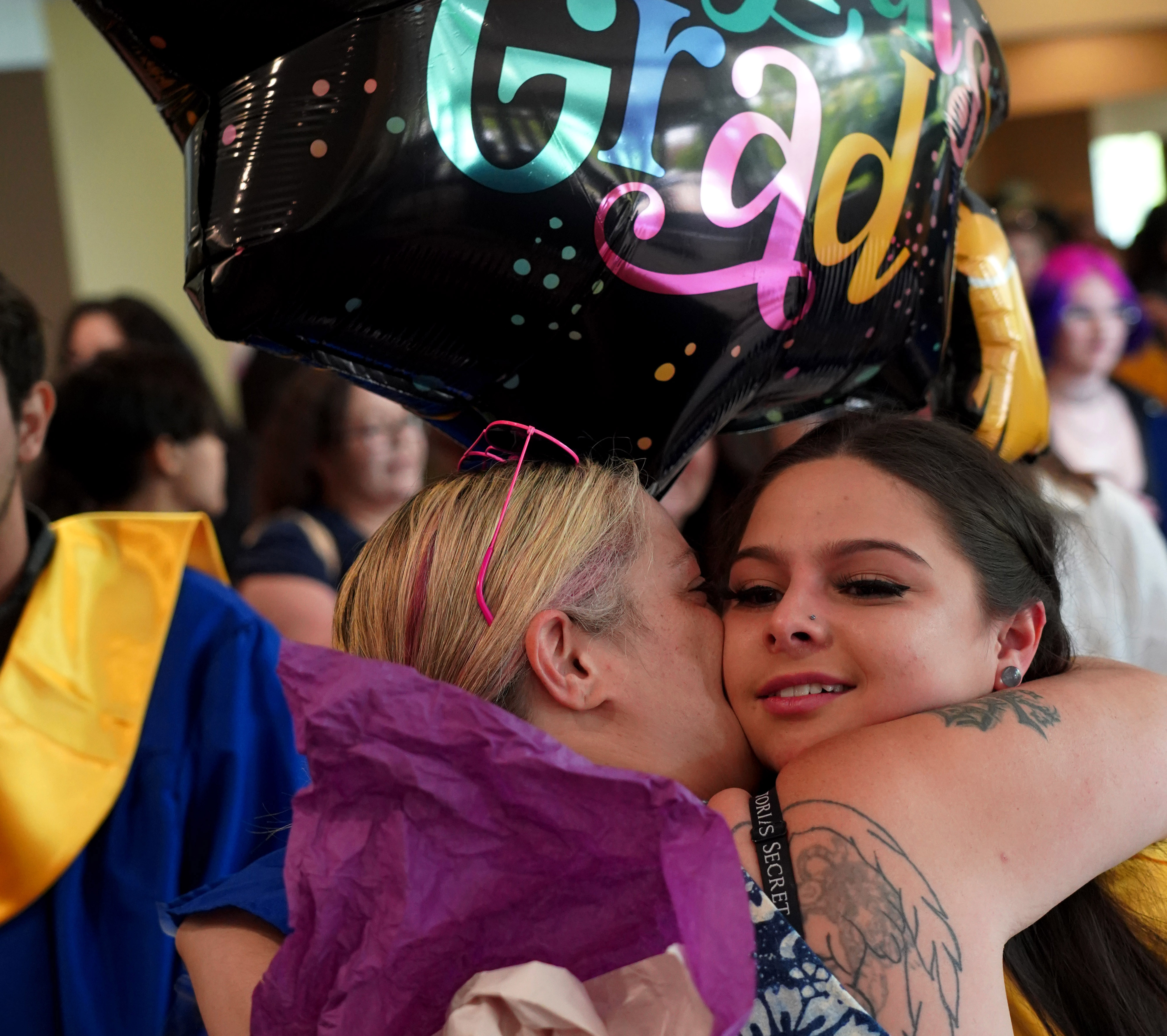 A PCA grad with balloons hugs a family member.