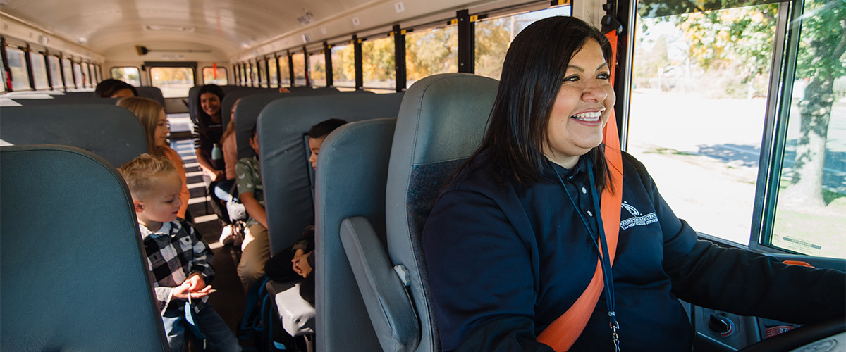 A bus driver in the driver's seat with kids in seats behind her. 