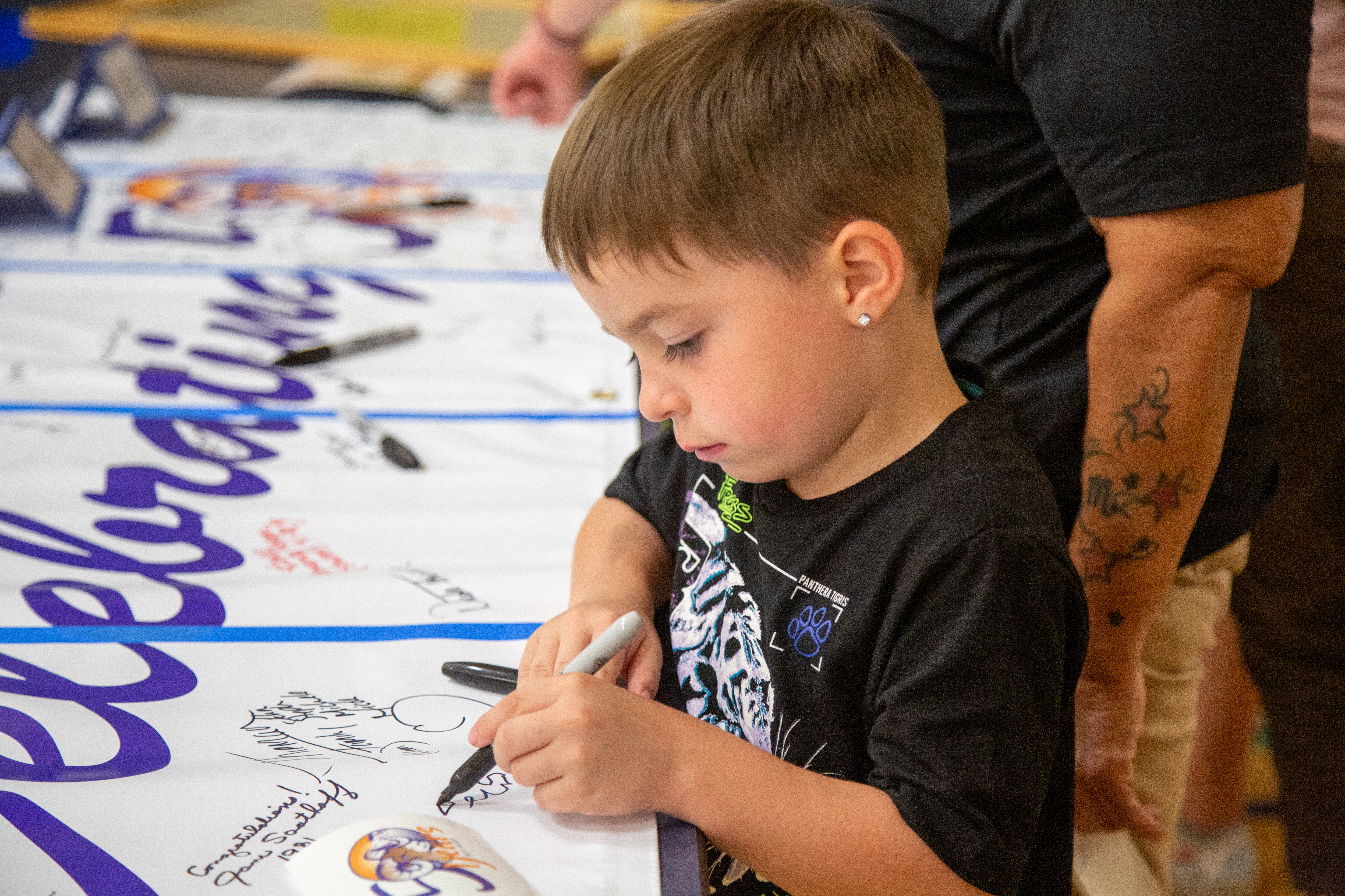 A young boy signs a "congratulations" sign at the school. 