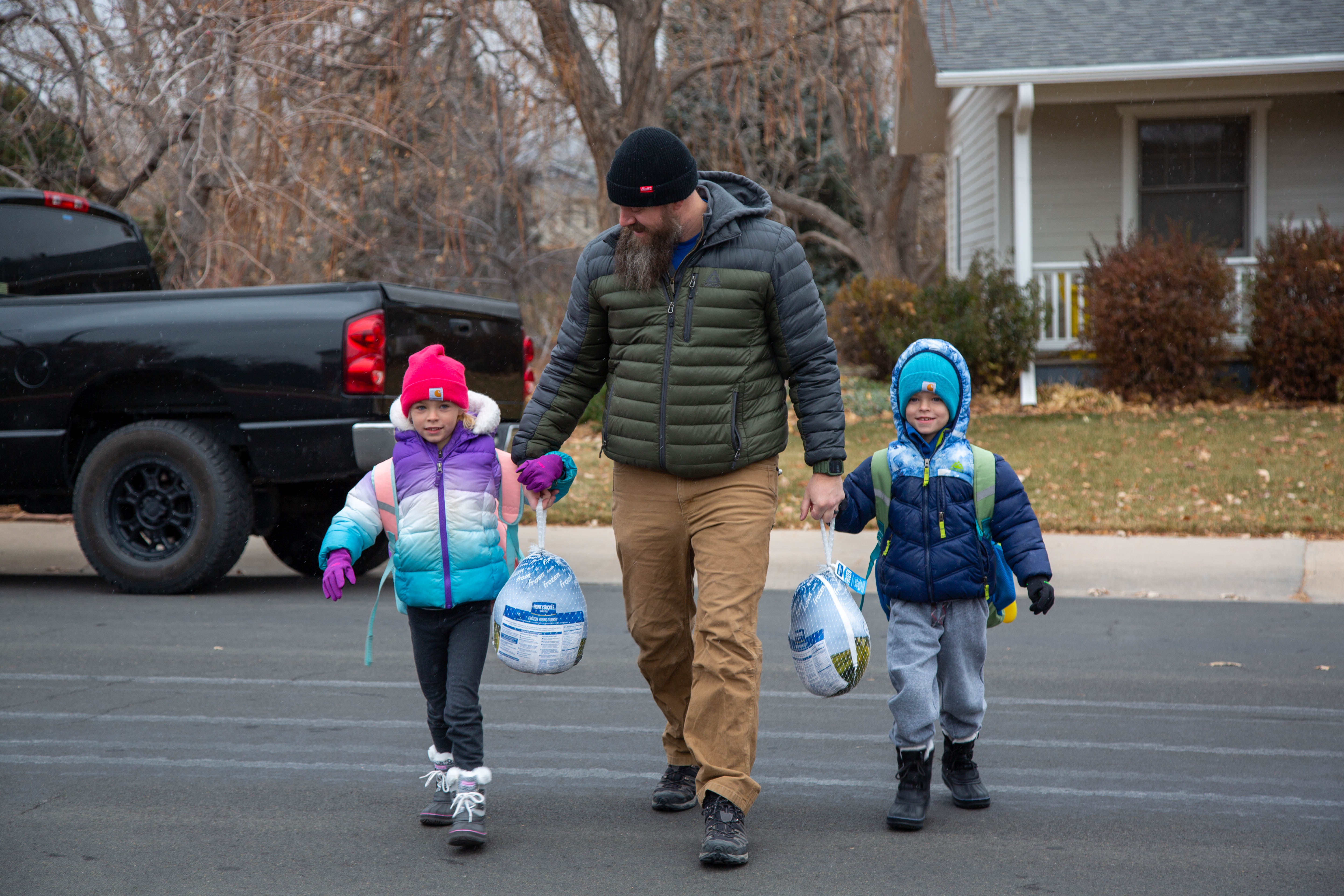 A dad holds hands with his two students, each holding turkeys. 