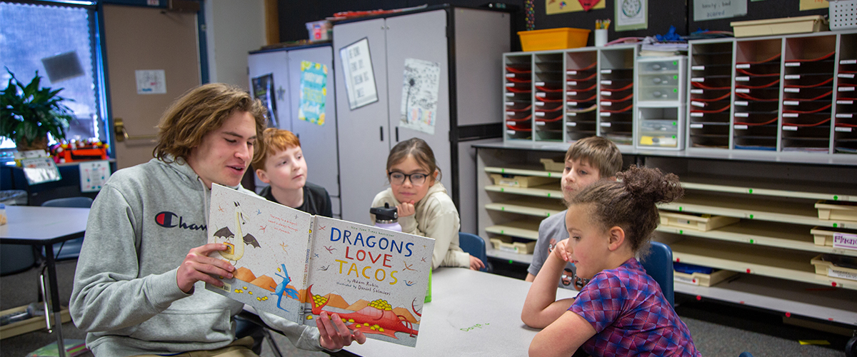 A high school student reads a book to younger students.