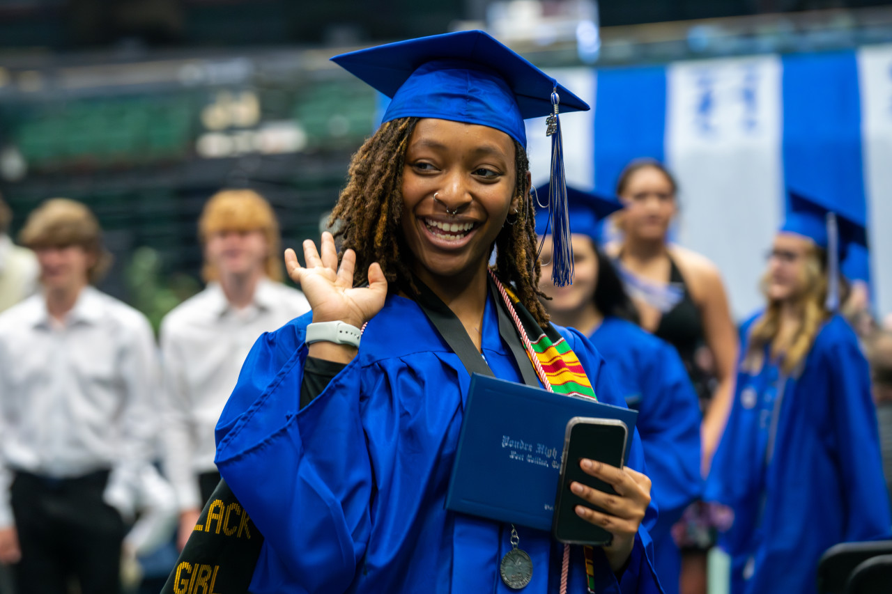 A PHS grad holding her diploma smiles at the camera. 