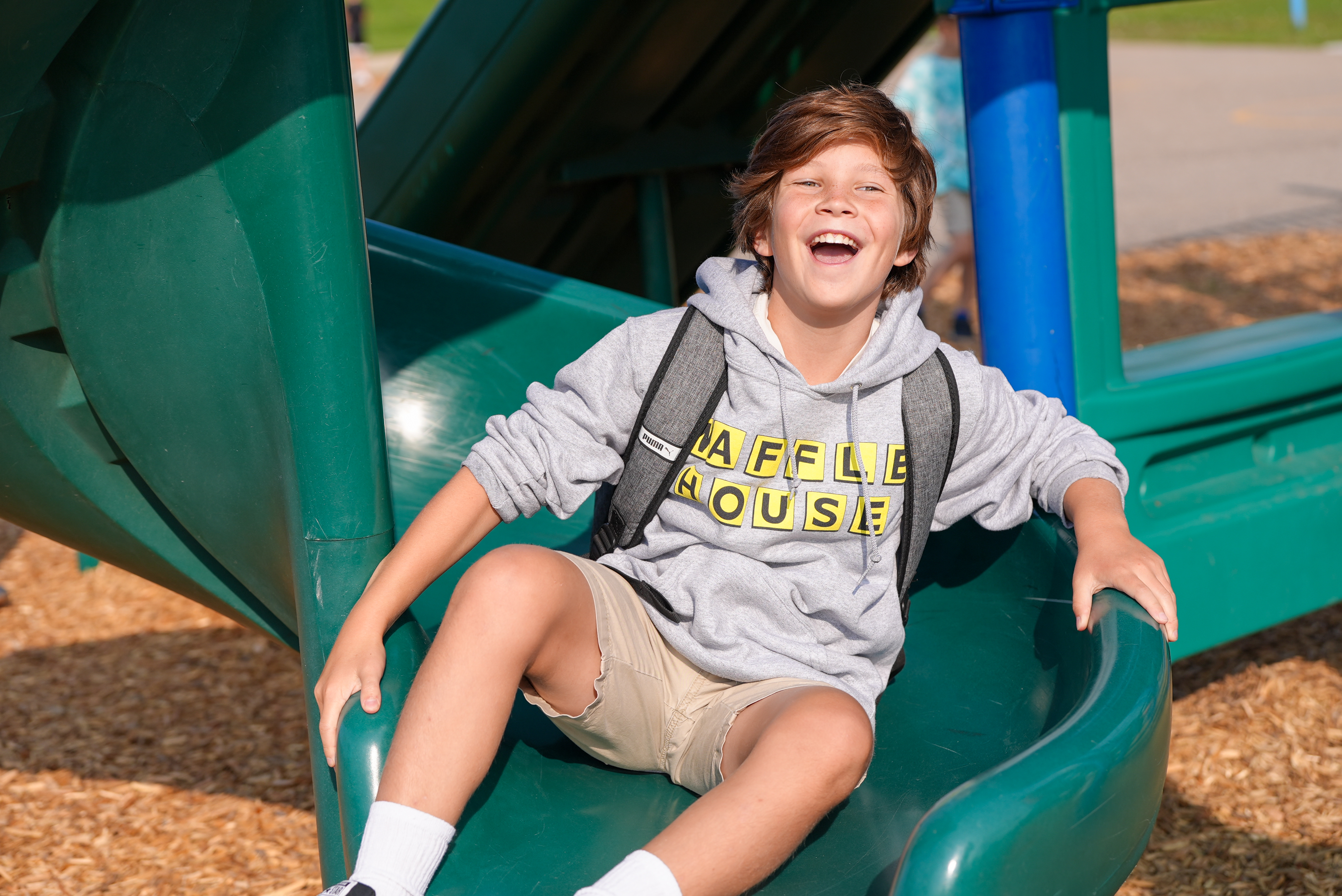 A boy smiles big while going down a slide. 