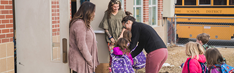 Parents saying goodbye to children outside a school.