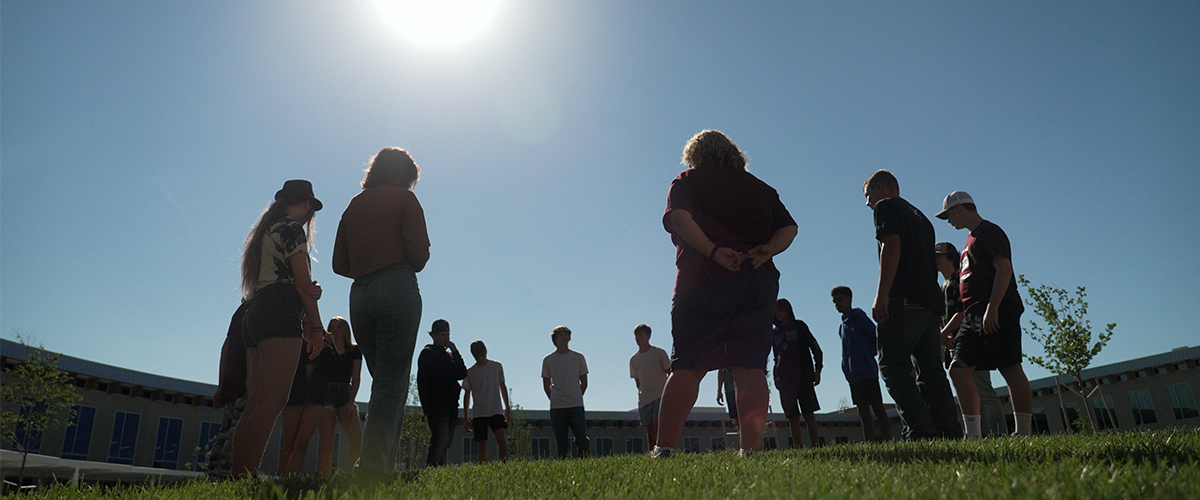 HIgh school student standing outside in a circle at dusk. 