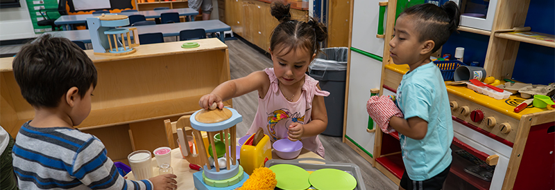 Preschoolers play in a toy kitchen area.