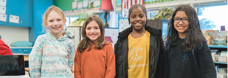 Four Dunn Elementary students in a classroom smile at the camera. 