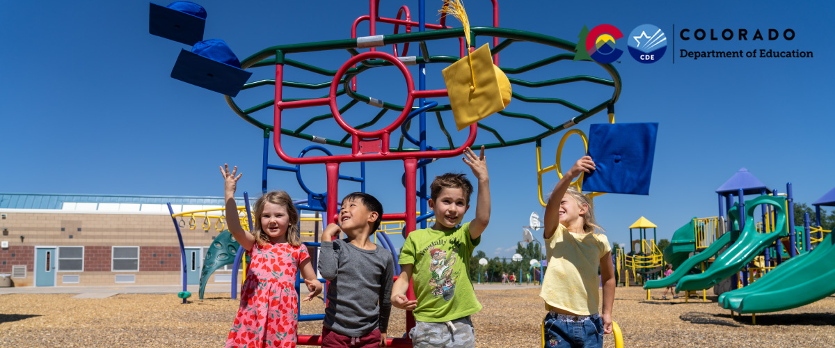 A group of young children throwing graduation caps in front of a playground