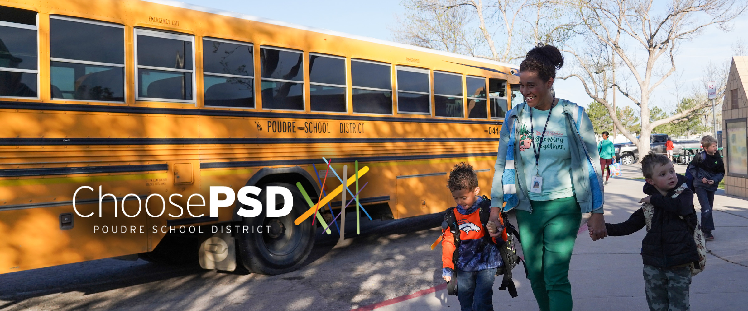 students and a staff member walking in front of a school bus smiling