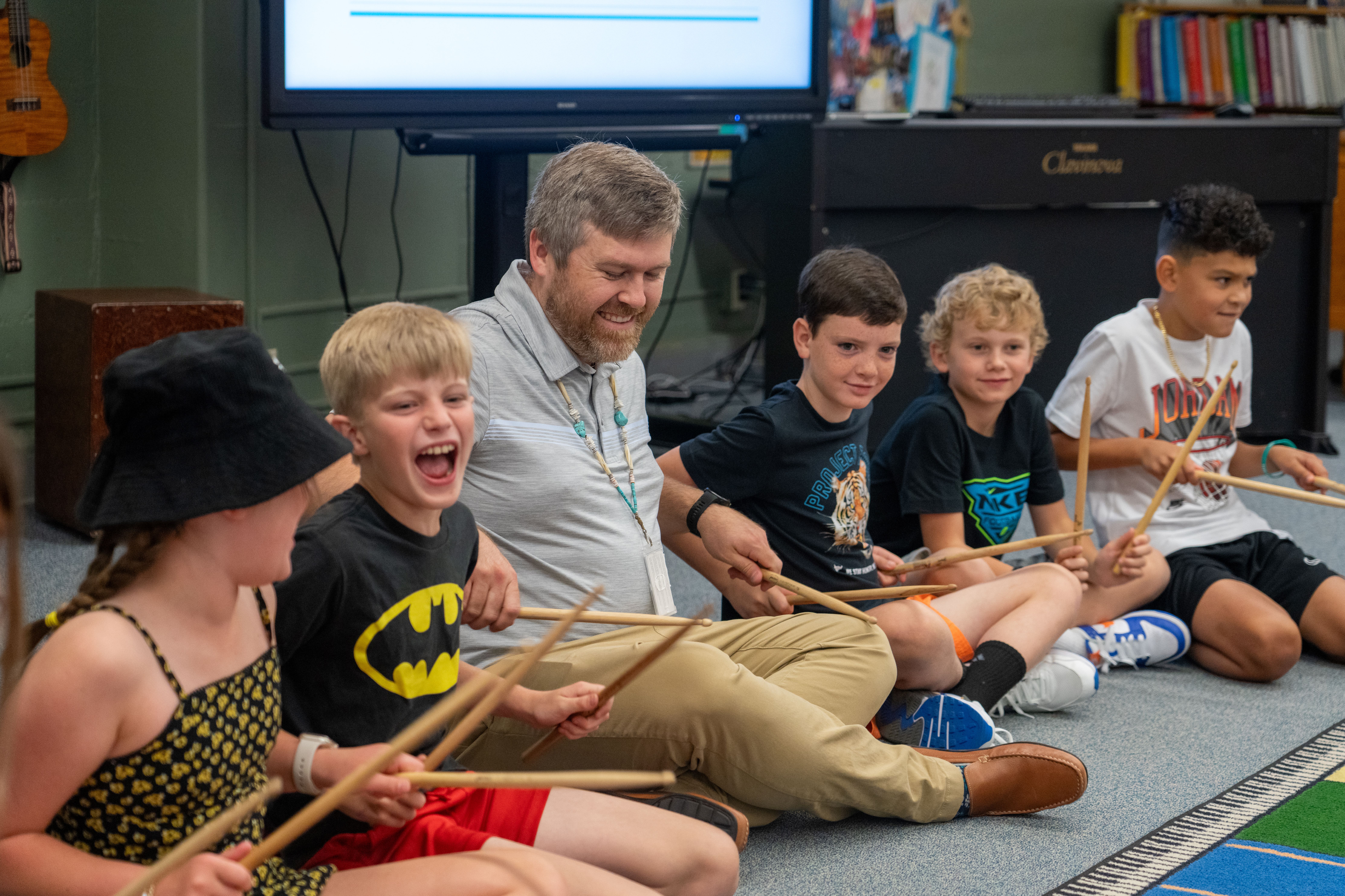 Josh Brink sits on the floor with students and musical instruments. 
