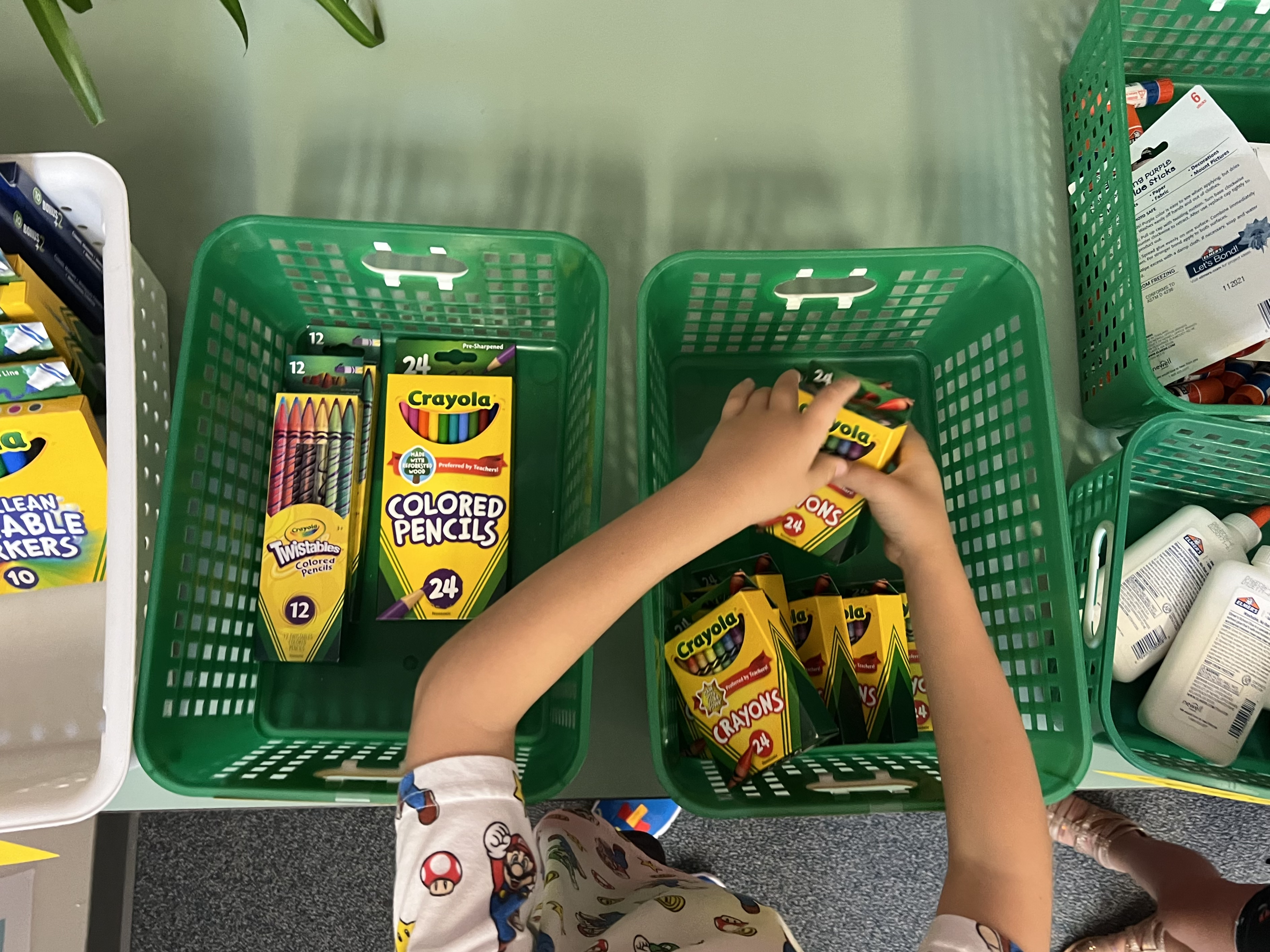 A child reaches in to bins of crayons, glue and other school supplies.