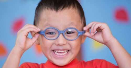 A smiling child holding the sides of his glasses on his head.