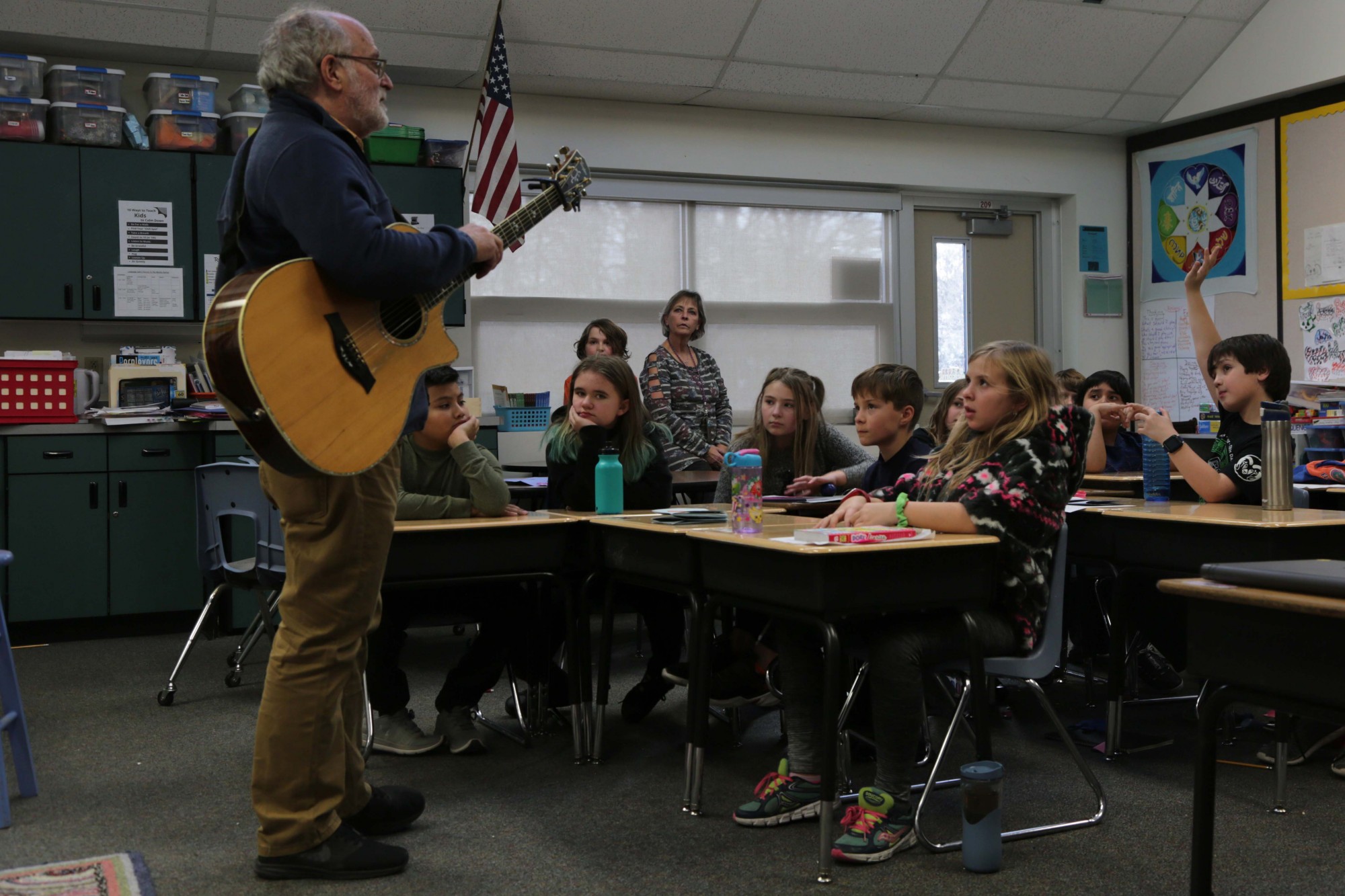 A man playing a guitar leads a Laurel class in writing a song.