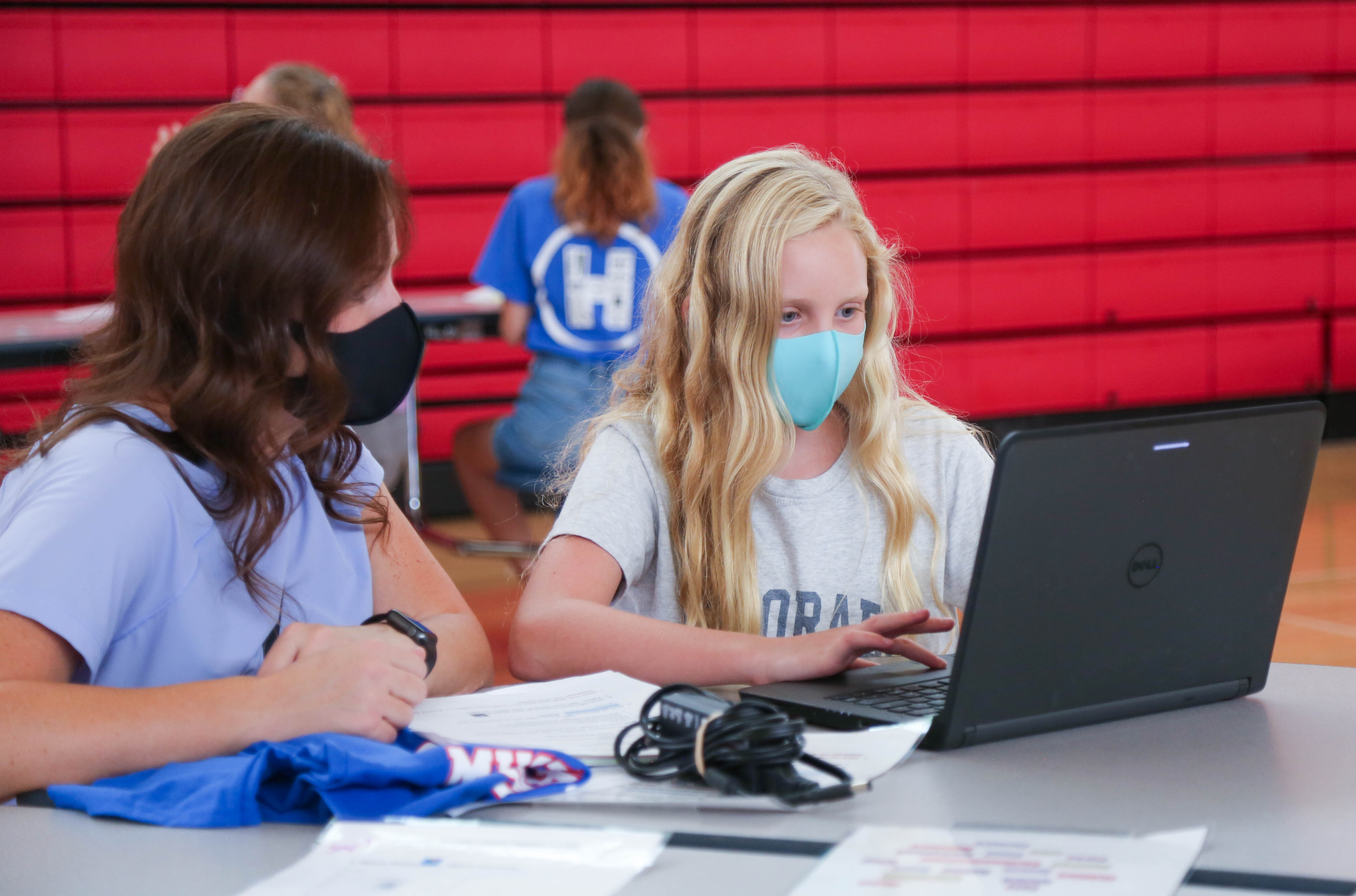 Students pick up laptops in a school gym. 