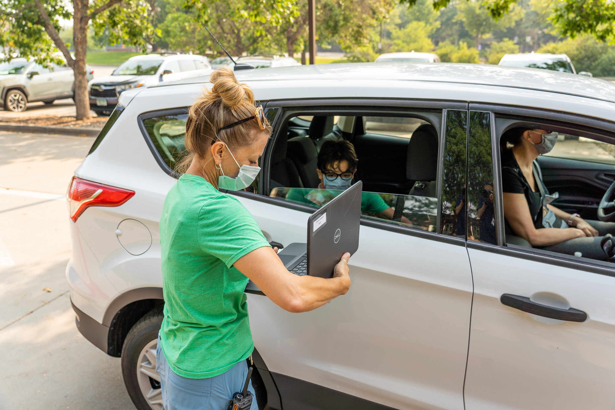A staff member hands a laptop to a family in a car.
