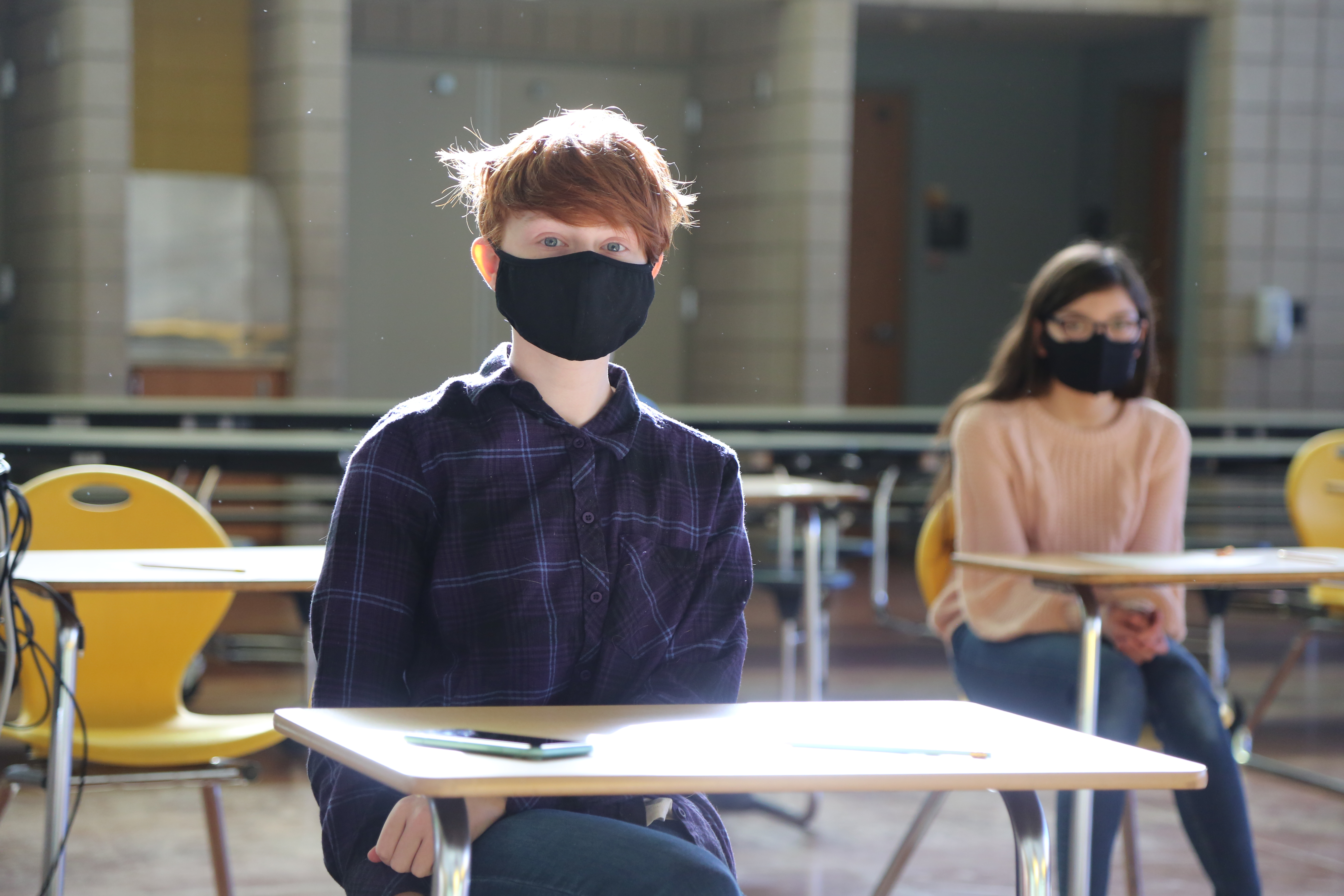 A student wearing a mask sitting at a classroom desk.