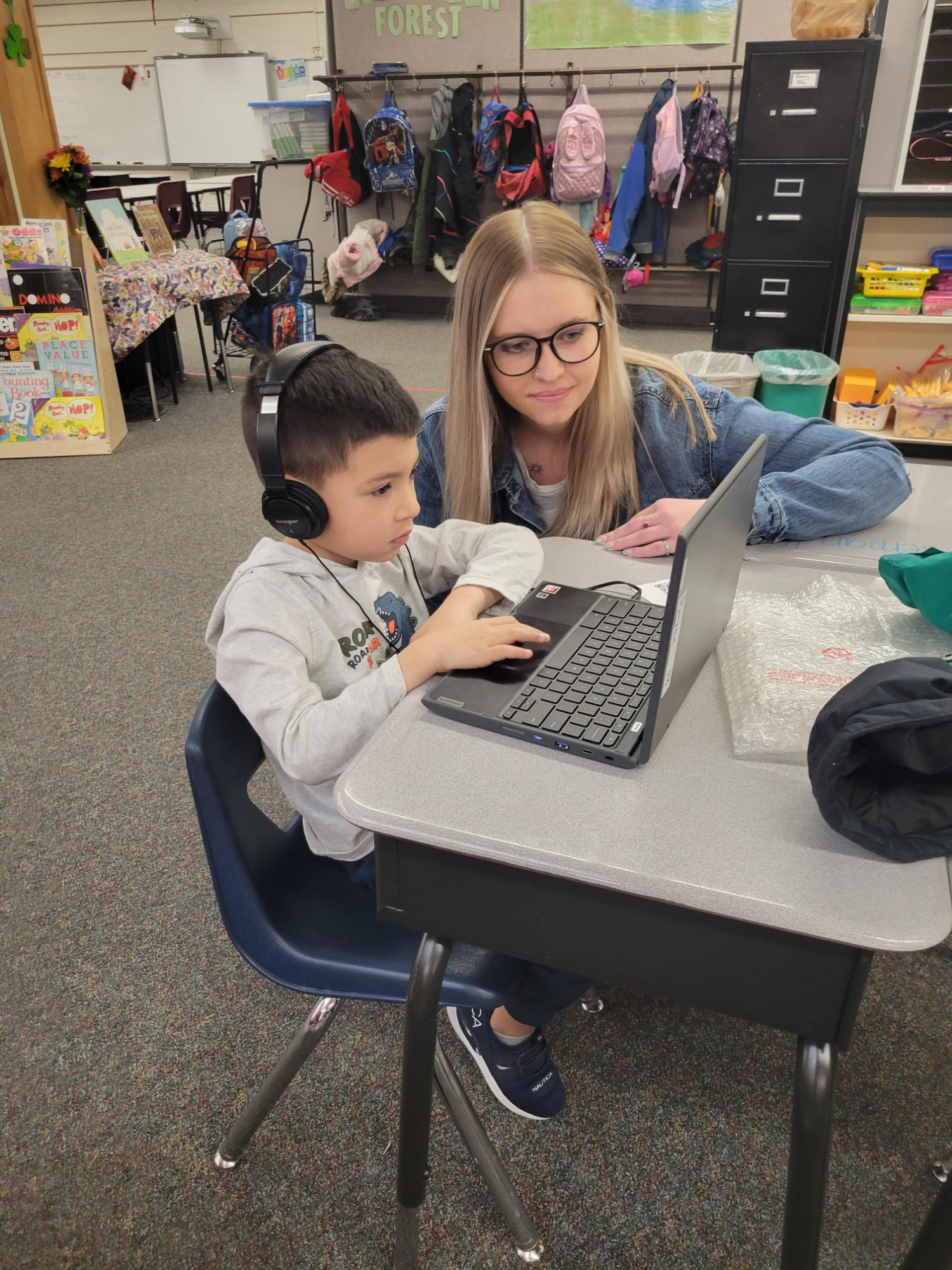 A student teacher helps a first grader at his desk.