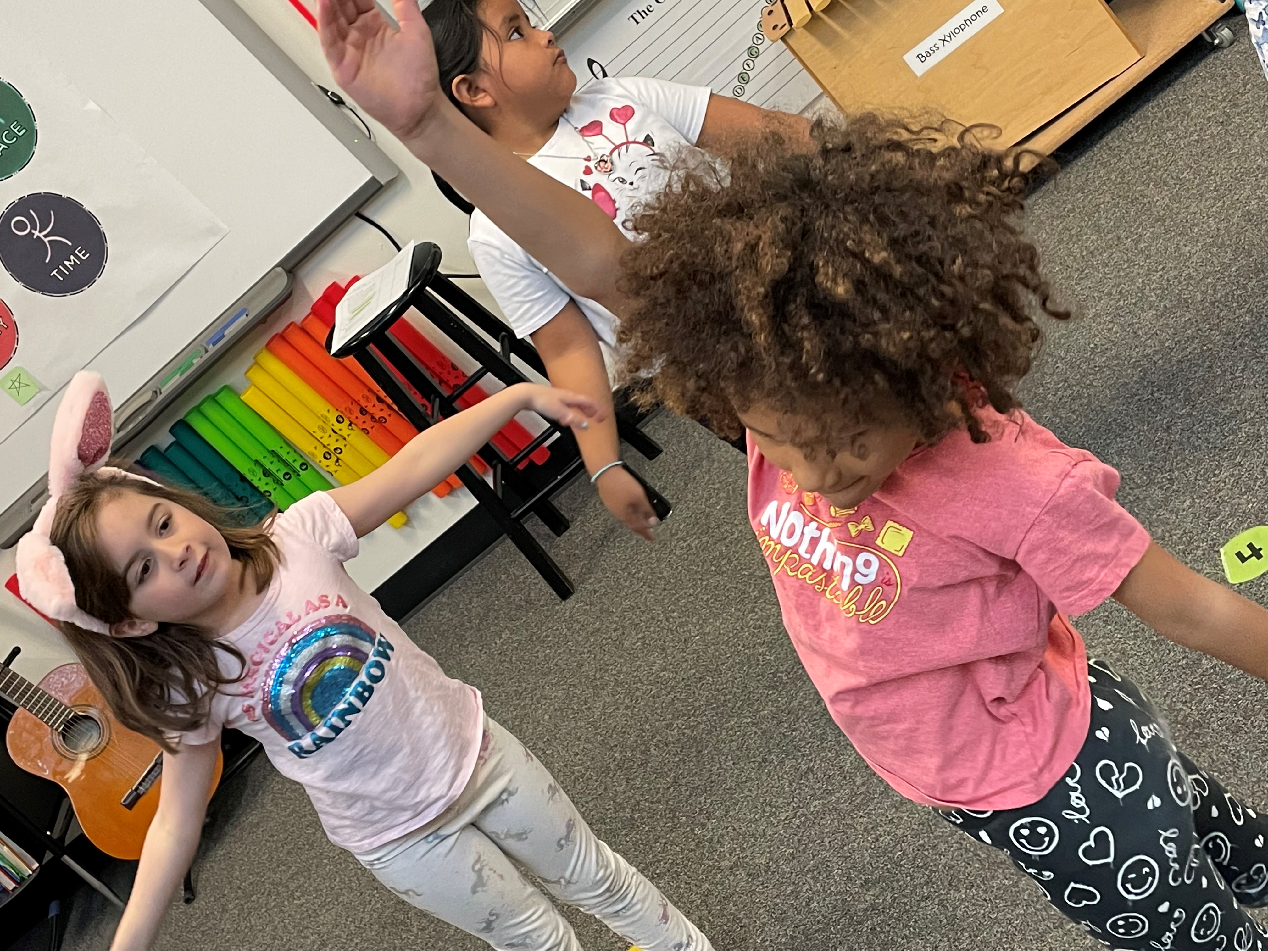 Two girls dance together in a classroom.