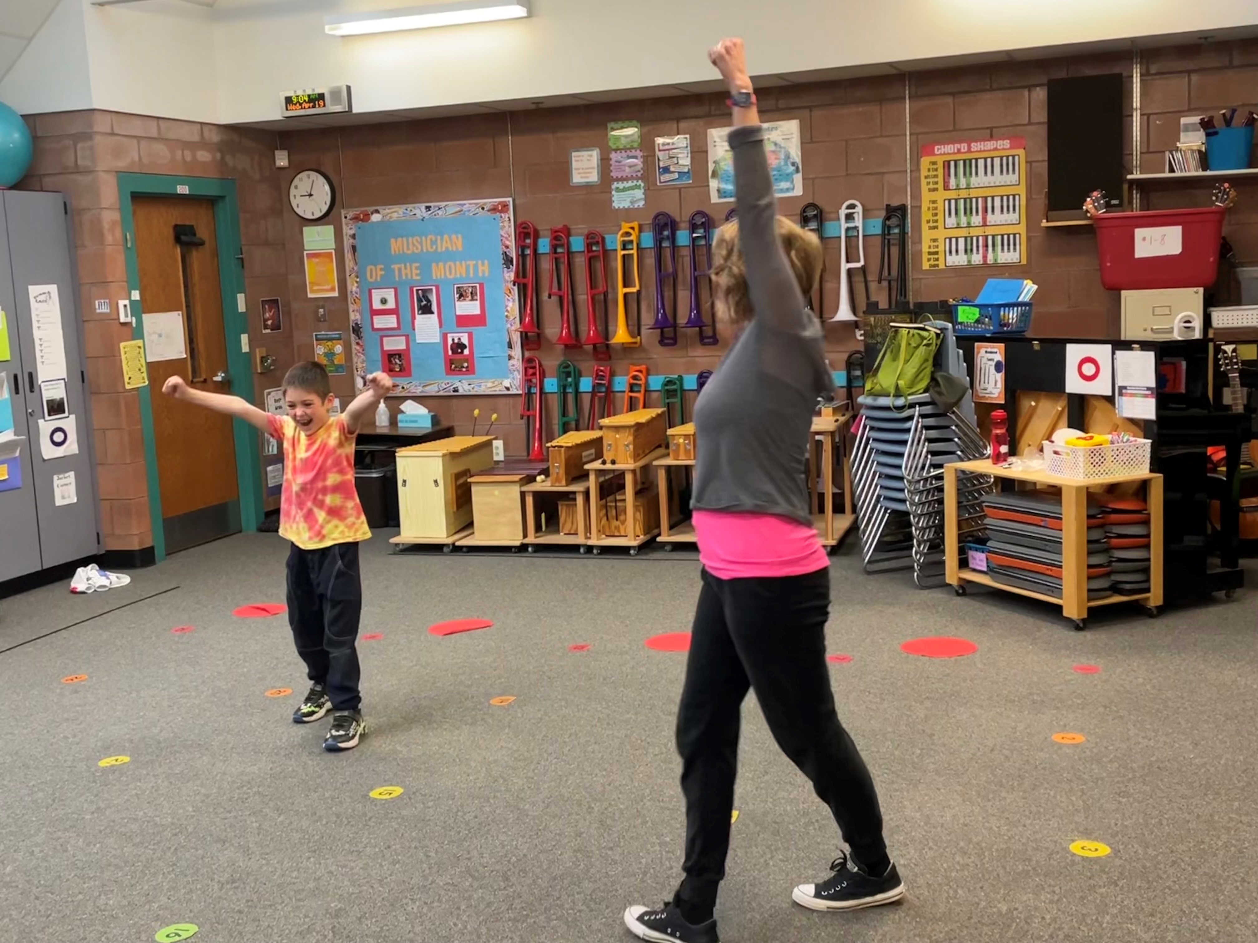 A young boy smiles while dancing near his teacher.