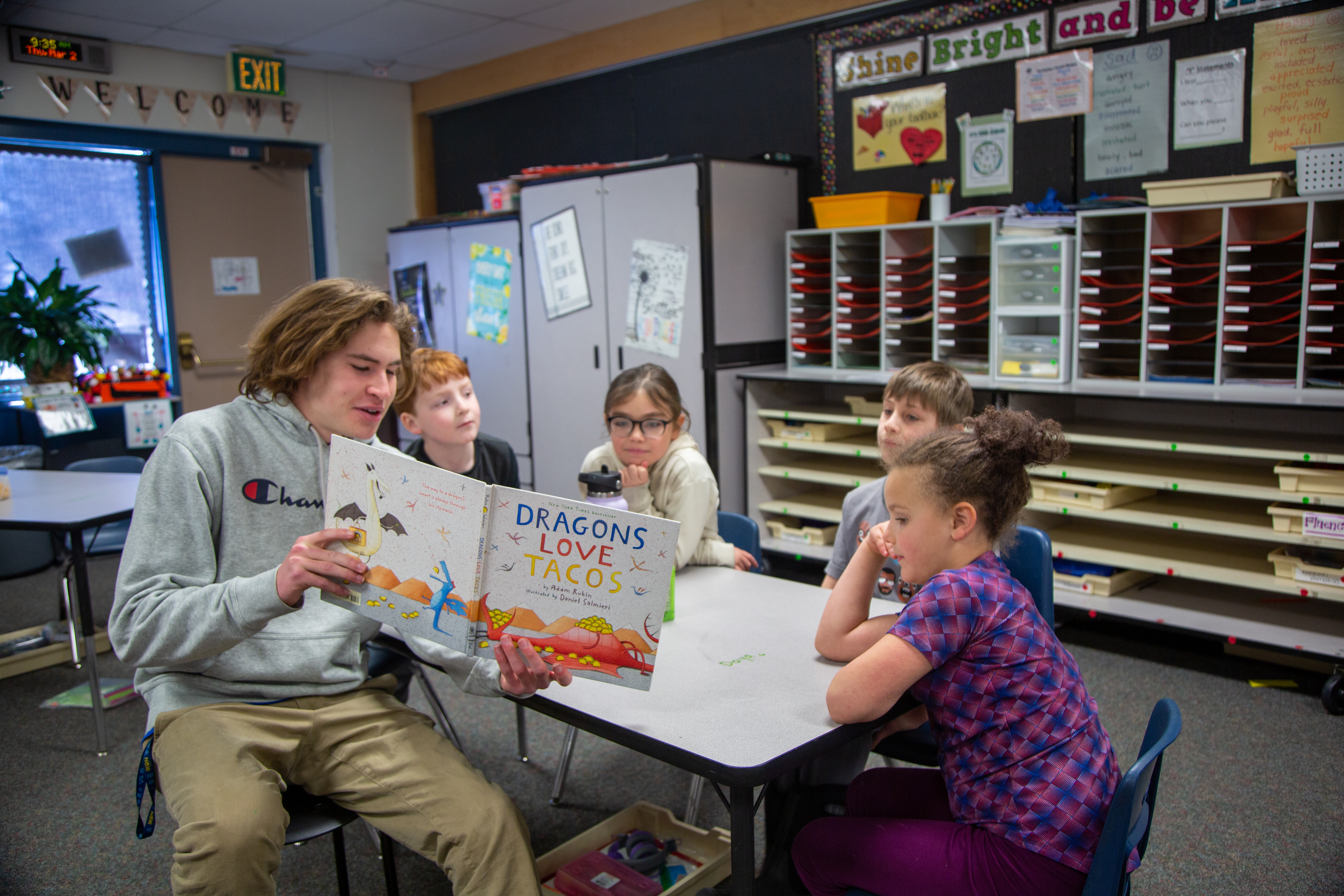 A high school student reads "Dragons Love Tacos" to students.