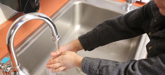 Hands being washed in a classroom sink.
