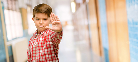 A middle school aged boy holding up his hand to say "stop."