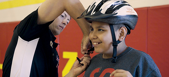 A man helps a student with his bike helmet.