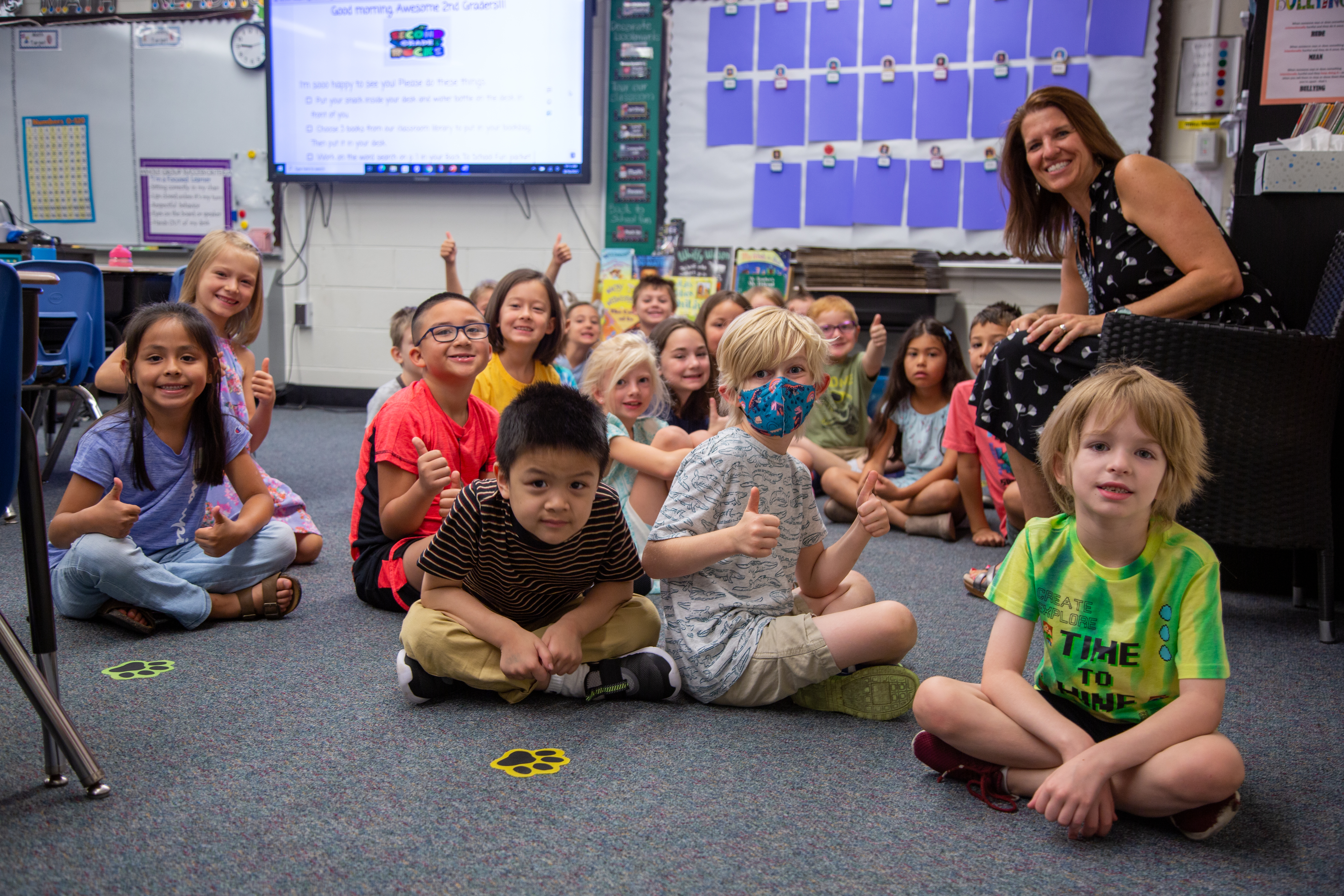 A teacher sits in a chair with young students on the rug. 