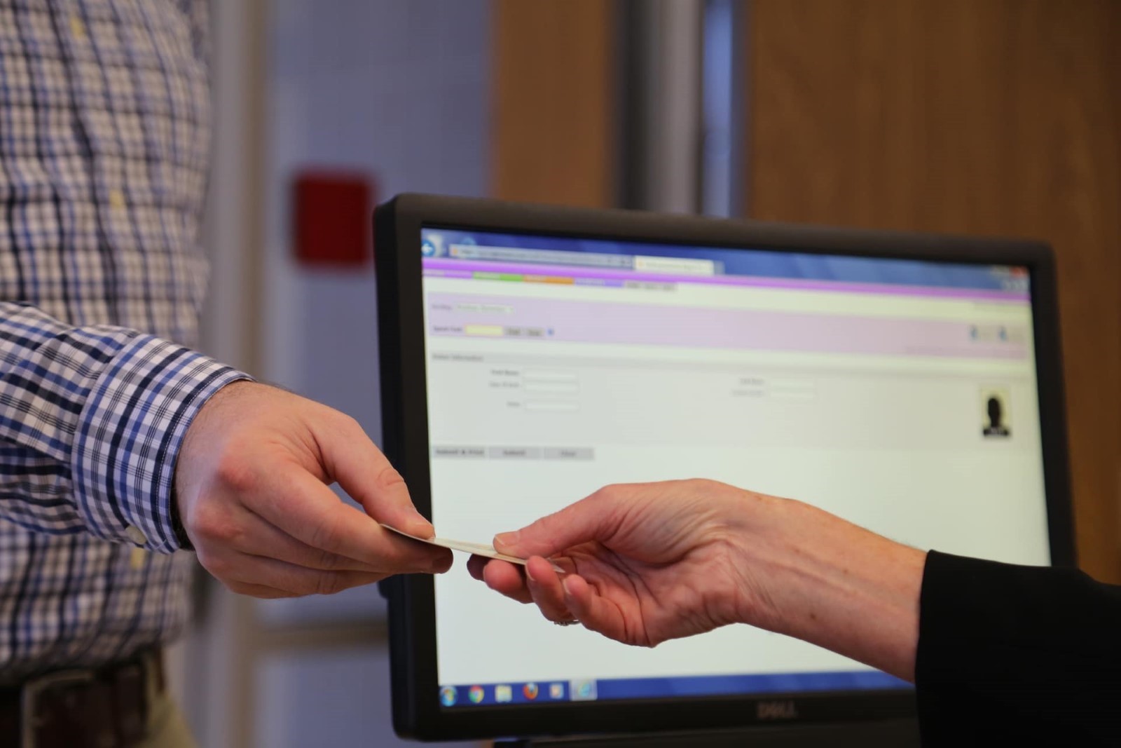 A hand with a card giving it to another hand. Computer screen in the background. 