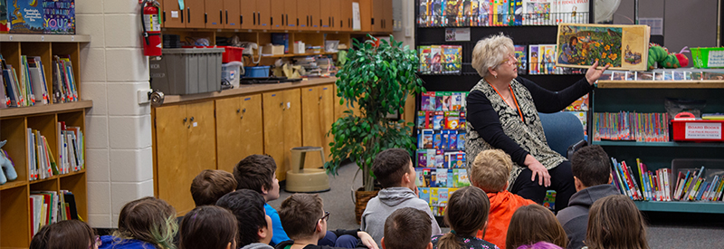 A volunteer reads to a sitting on the floor in a classroom. 