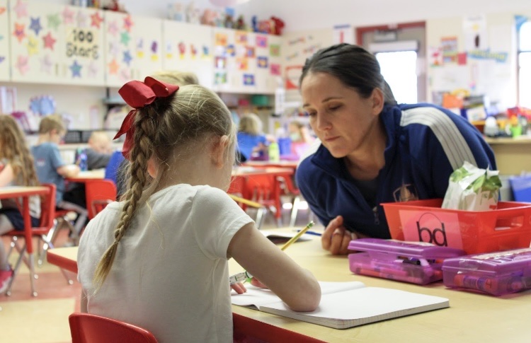 A teacher works with a kindergartner at a table.