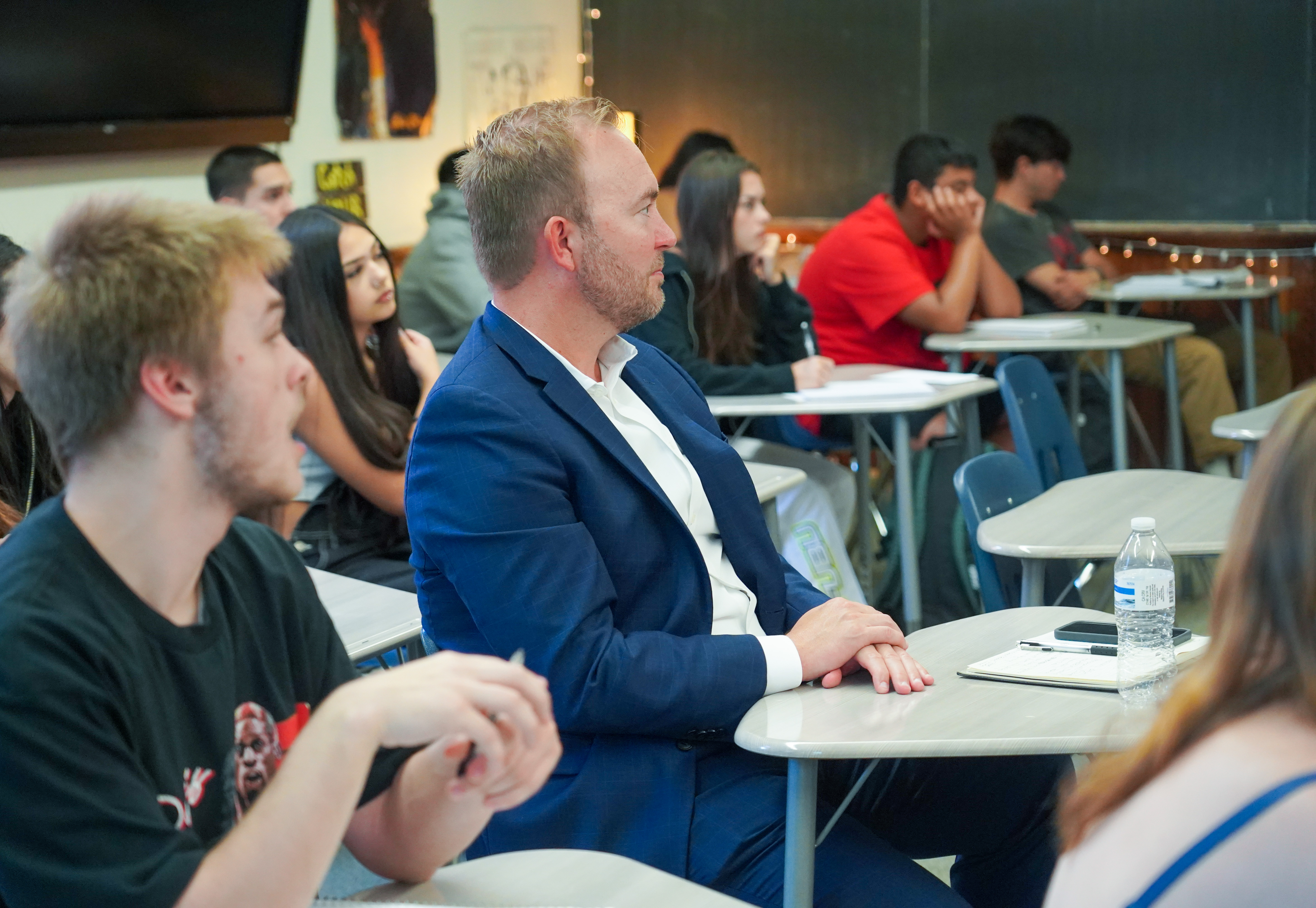 Superintendent Kingsley sits with high school students listening to the teacher.. 