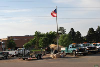 Maintenance vehicles outside a school with a flag pole.