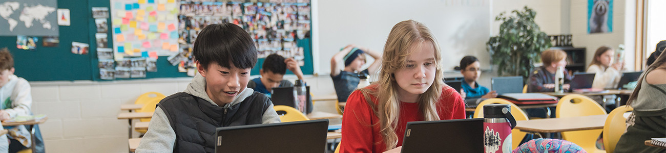 Two middle school students work at their desks. 