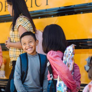 Smiling kids stand outside a school bus. 