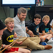 Josh Brink, music teacher, sits with students on the floor. 