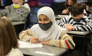 A Dunn elementary student who is wearing a hijab smiles from her desk.